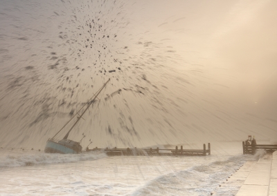 Waves crashing against the sea defences atsunrise with a stranded yacht in the background